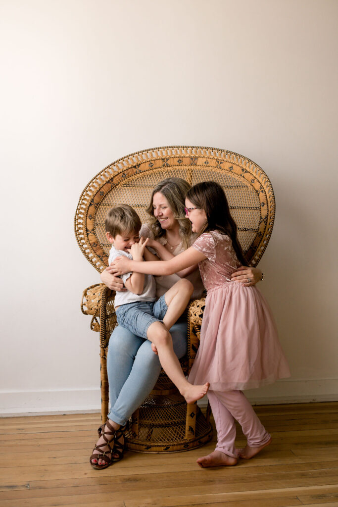 mom sitting on a chair with son in her lap, daughter standing beside