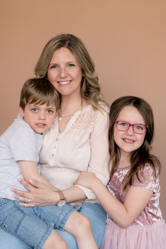 mom sitting, with son on her lap, daughter snuggled up on her arm, all looking and smiling at the camera