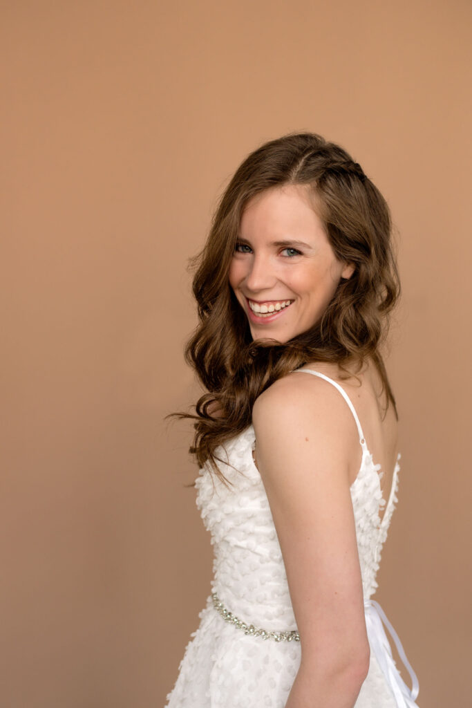 bride looking over shoulder with a big radiant smile. Hair is curled with a little side braid