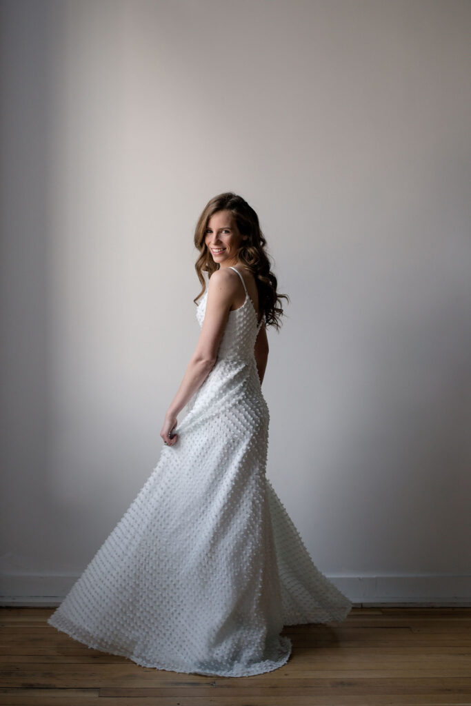 Bride is twirling, looking over her shoulder at the camera, with a coy smile.