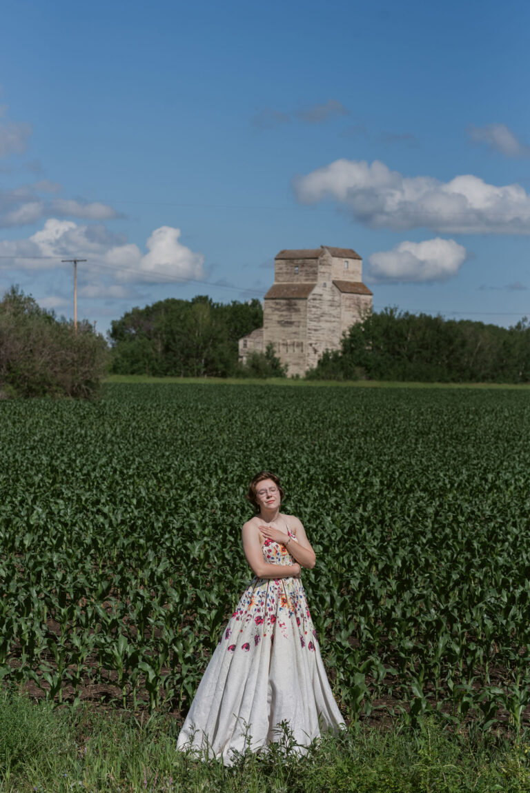 graduate standing in field with grain bin in the background